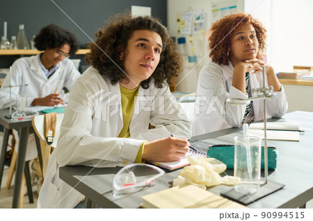 Clever intercultural students of highschool in labcoats listening to teacher 90994515