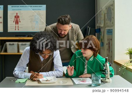 Mature male teacher of anatomy bending over two students during frog dissection 90994548