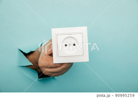 Male hand holds socket in torn hole of blue background 90995259
