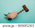 Hand holding a judge's gavel through torn blue paper wall. Law and courts, triumph of justice 90995263