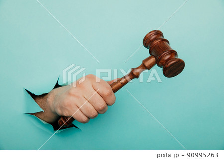 Hand holding a judge's gavel through torn blue paper wall. Law and courts, triumph of justice 90995263