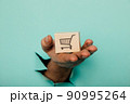 Hand with a delivery box through a blue paper hole 90995264