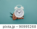 Hand holds alarm clock through a blue paper hole. Time management and deadline concept 90995268