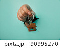 Man's hand with house key through a hole in blue background. House sale and rent concept 90995270