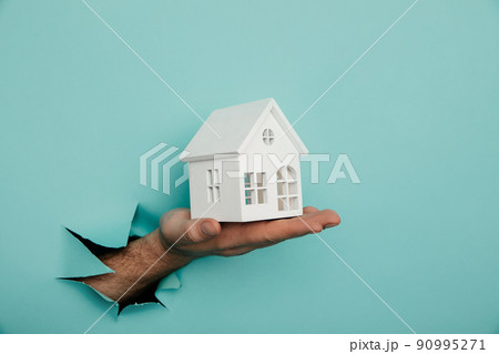 Man's hand with house through a hole in blue paper. House sale and rent concept 90995271