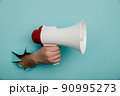 Man's hand arm hold megaphone isolated through torn blue background 90995273