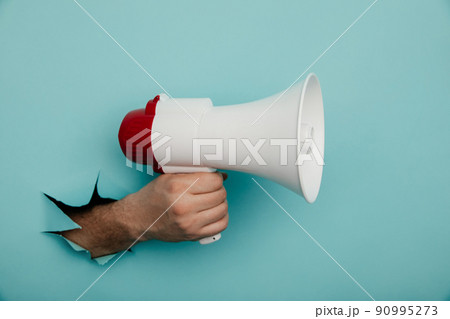 Man's hand arm hold megaphone isolated through torn blue background 90995273