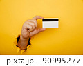 Male hand is holding credit bank card in torn hole of yellow background. Online shopping, purchasing products concept. 90995277
