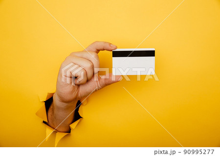 Male hand is holding credit bank card in torn hole of yellow background. Online shopping, purchasing products concept. 90995277