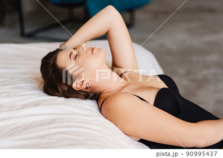 an attractive brunette woman in a black bodysuit by the bed in the bedroom. an attractive brunette woman in a black bodysuit by the bed in the bedroom. 90995437