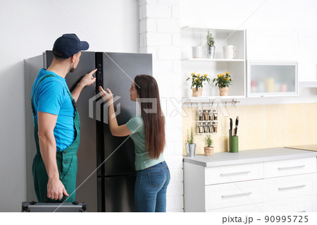 Male technician talking with client near refrigerator in kitchen Male technician talking with client near refrigerator in kitchen 90995725