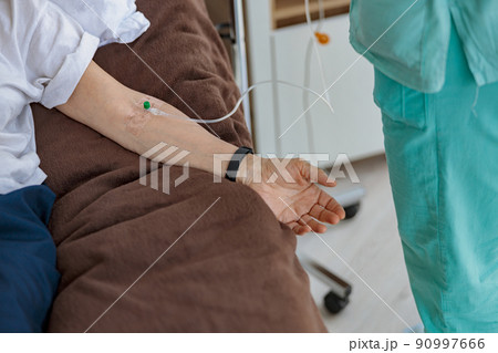 Nurse putting a drip in the arm of her patient in modern medical clinic 90997666