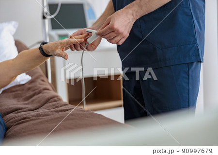 Nurse checking with fingertip pulse oximeter oxygen saturation of patient blood in hospital 90997679