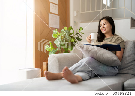 happy asian young woman sitting on sofa and reading book at home -people and leisure concept 90998821