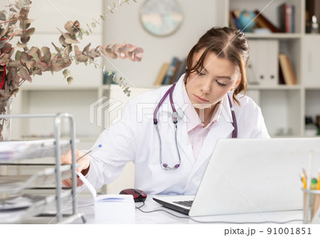 Positive woman doctor sitting at workplace with computer in office Positive woman doctor sitting at workplace with computer in office 91001851