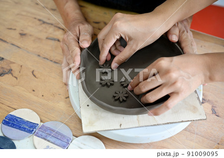 Top view image, Hands making a clay pottery, decorating a clay plate on worktable Top view image, Hands making a clay pottery, decorating a clay plate on worktable 91009095