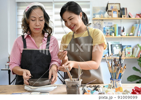 Young asian ceramic craftsman teacher teaching aged female student to making a clay bowl Young asian ceramic craftsman teacher teaching aged female student to making a clay bowl 91009099