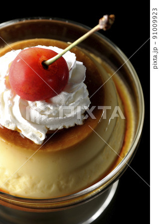 サンデーカップに盛り付けてある生クリーム、チェリーの乗った昔ながらのレトロプリンを黒背景で俯瞰撮影 91009923