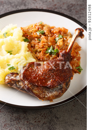 Romanian Rata pe varza duck leg serving with mashed potatoes and stewed cabbage close-up in a plate. Vertical 91012498