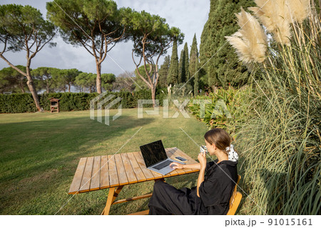 Girl use laptop and drink tea at table on lawn 91015161