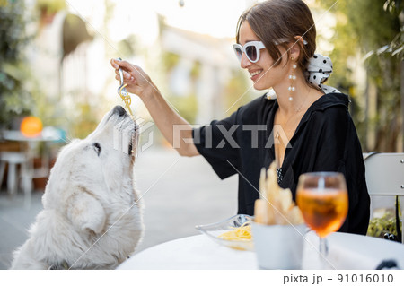 Woman eating pasta with her cute white dog at the restaurant 91016010