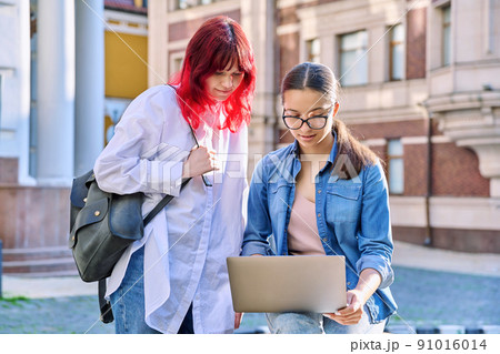 Two teenage female students using outdoor laptop, city street background 91016014