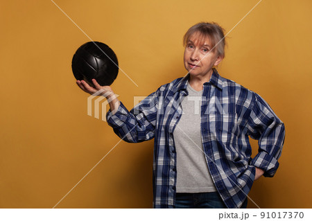 Portrait of senior woman holding soccer ball against yellow studio wall background 91017370