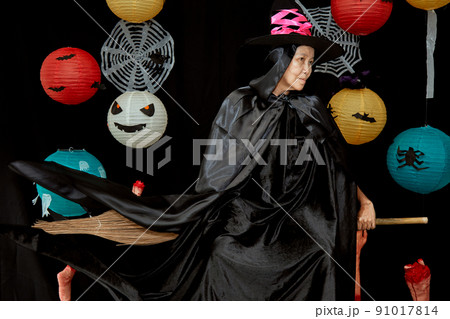 Senior woman in witch costumes celebrating Halloween posing on broom over bats and spider web 91017814