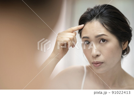 鏡を見ながら生え際を気にするアラフィフの女性 91022413
