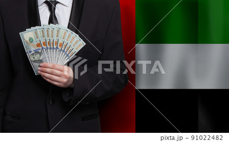 Hand giving 100 US dollar bills money banknotes against flag of United Arab Emirates background 91022482