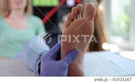 Doctor podiatrist in sterile gloves examining female foot Doctor podiatrist in sterile gloves examining female foot 91023167