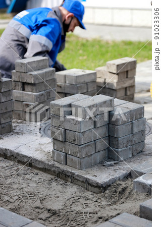 Bricklayer in work clothes sits on sidewalk and lays out paving slabs. Sight of working man in open Bricklayer in work clothes sits on sidewalk and lays out paving slabs. Sight of working man in open 91023306