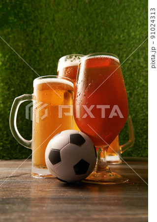 Four glasses of beer with soccer ball on the green grass background. 91024313
