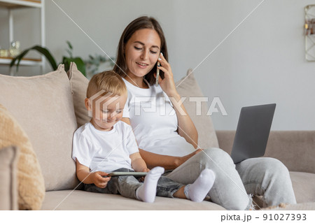 mom and son at home in the living room. parenting and business for a young European mom. A woman is working on a laptop and playing with her son 91027393