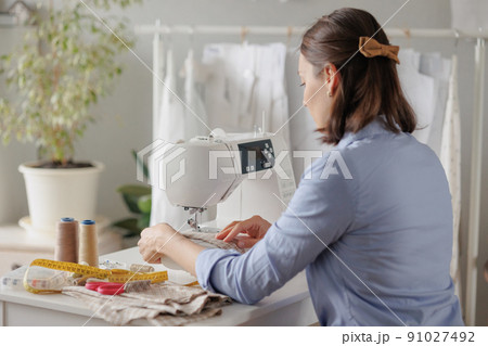 woman sews clothes on a sewing machine in a workshop. work in the production of clothing and textiles. patterns and fabrics for sewing 91027492