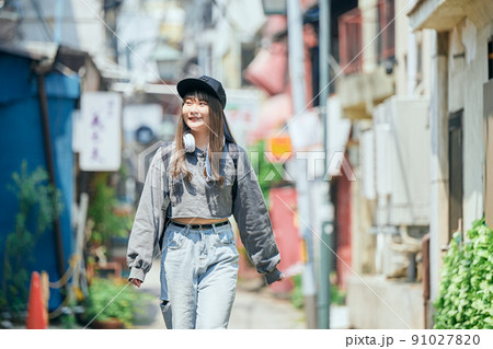 ヘッドフォンを首にかけて歩くZ世代の女性 91027820