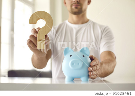 Man who is thinking about what currency to keep money holds question mark near piggy bank. Man who is thinking about what currency to keep money holds question mark near piggy bank. 91028461