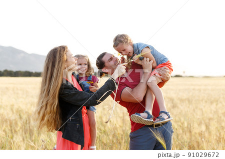 Happy family father of mother and two daughters sisters on nature at sunset.Carefree parents having fun with their kids on a field. 91029672