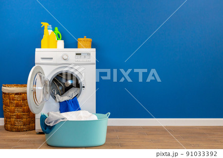 Washing machine with laundry on blue wall background Washing machine with laundry on blue wall background 91033392