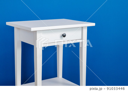 White wooden nightstand table against blue wall White wooden nightstand table against blue wall 91033446