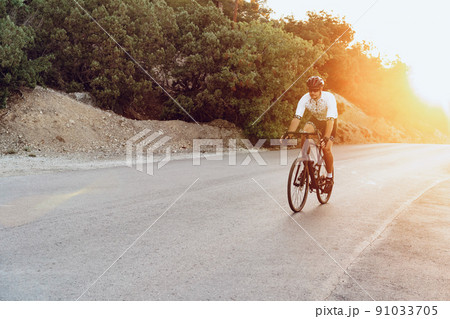 Man cyclist pedaling on a road bike outdoors in sun set 91033705