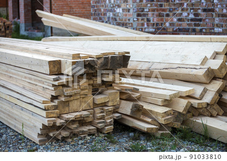 Stack of natural brown uneven rough wooden boards on building site. Industrial timber for carpentry, building, repairing and furniture, lumber material for roofing construction. 91033810