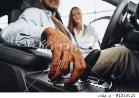Young attractive woman salesperson in car showroom showing a car to her male client 91033929