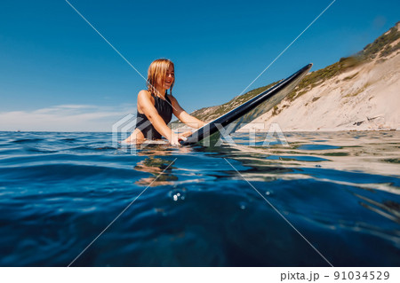 Portrait of young blonde surf girl in ocean during surfing. Woman on surfboard 91034529