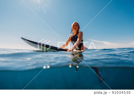 Attractive surf girl sit on surfboard in ocean. 91034530