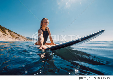 Sunny day with attractive surf girl on surfboard in ocean. Beautiful young woman look at camera Sunny day with attractive surf girl on surfboard in ocean. Beautiful young woman look at camera 91034539