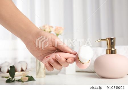 Woman holding face cleansing brush over white table, closeup. Cosmetic accessory 91036001