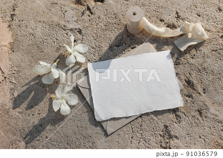 Blank greeting card, invitation mockup. White oleander flowers. Grunge sandstone, concrete backgound, ribbon in sunlight. Modern wedding template stationery. Summer, vacation design.Flat lay, top view 91036579
