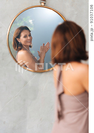 an attractive woman admires her reflection in a round mirror. an attractive woman admires her reflection in a round mirror. 91037106