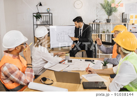 Five multiracial partners working with blueprints at office sitting near big digital screen. 91038144